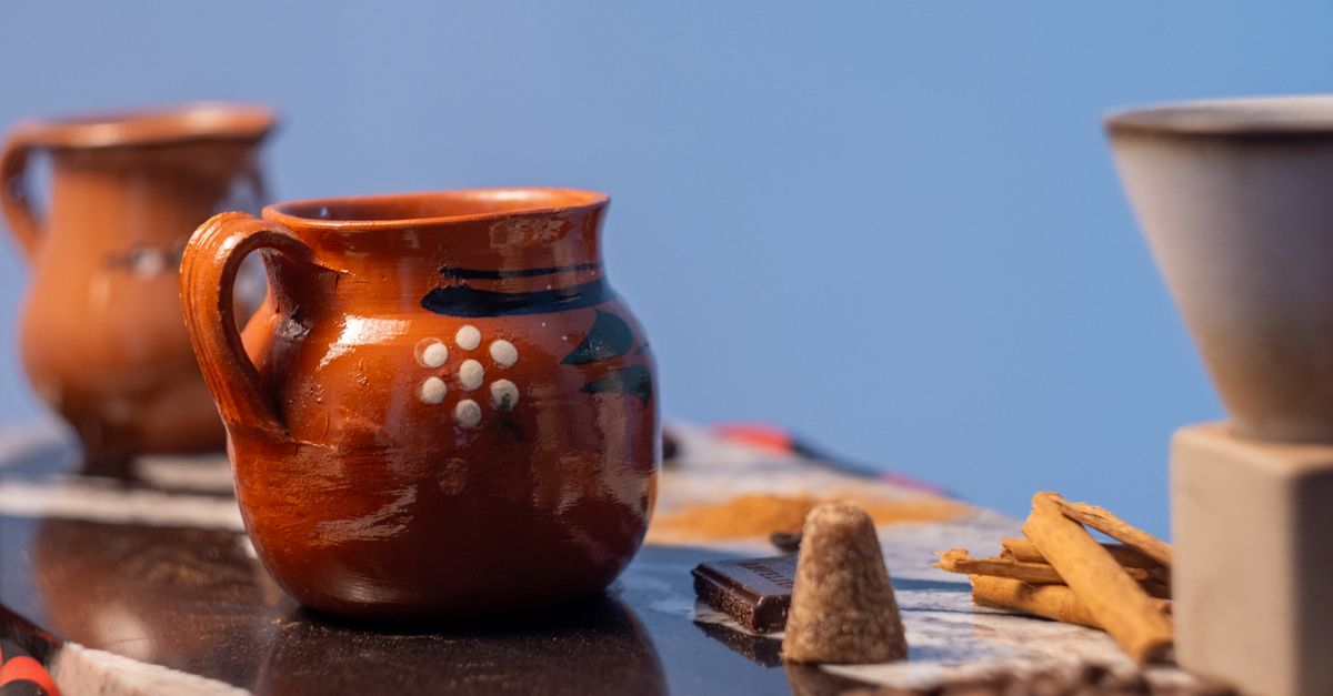 Olla de barro humeante sobre mesa de madera junto a una ventana con luz natural